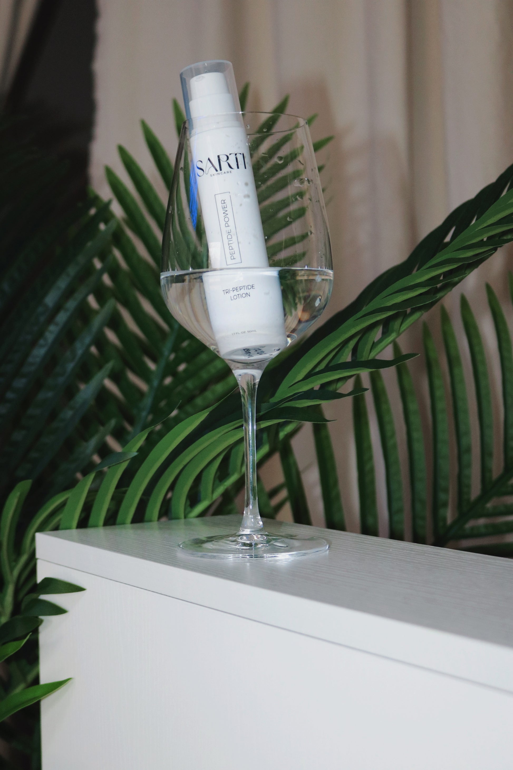 Skincare bottle on a glass stand with green leaves in the background