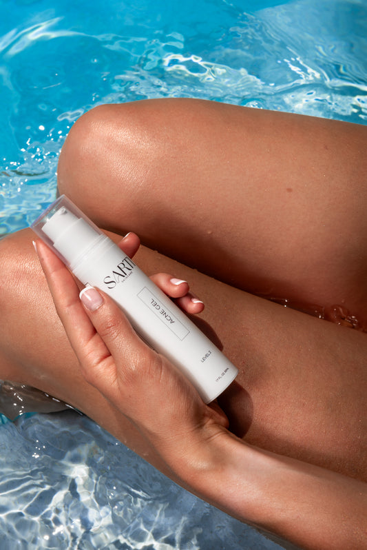 Person holding a bottle of acne gel treatment cream by a pool